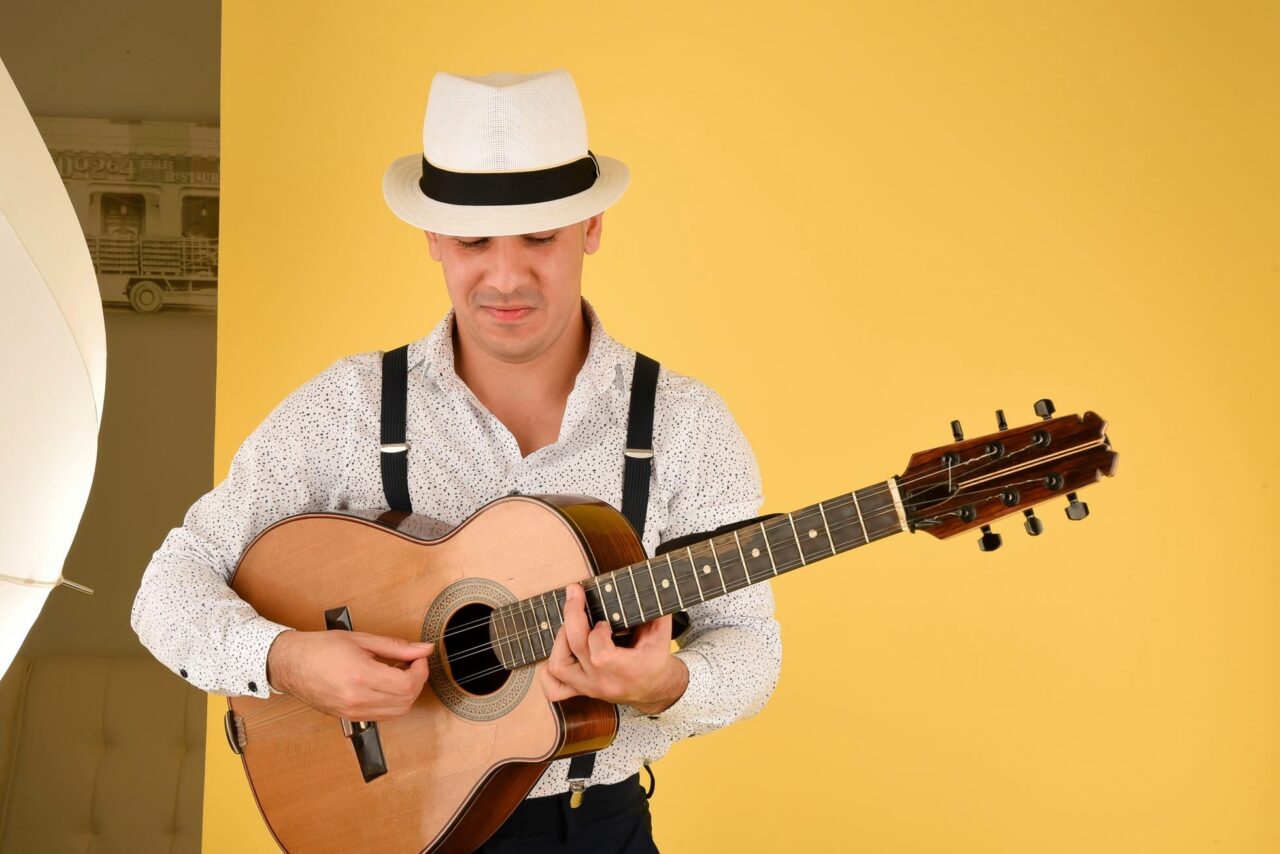 Guitar artist with Cuban hat on Infront of a bright yellow wall with guitar in hand at Hotel Haya