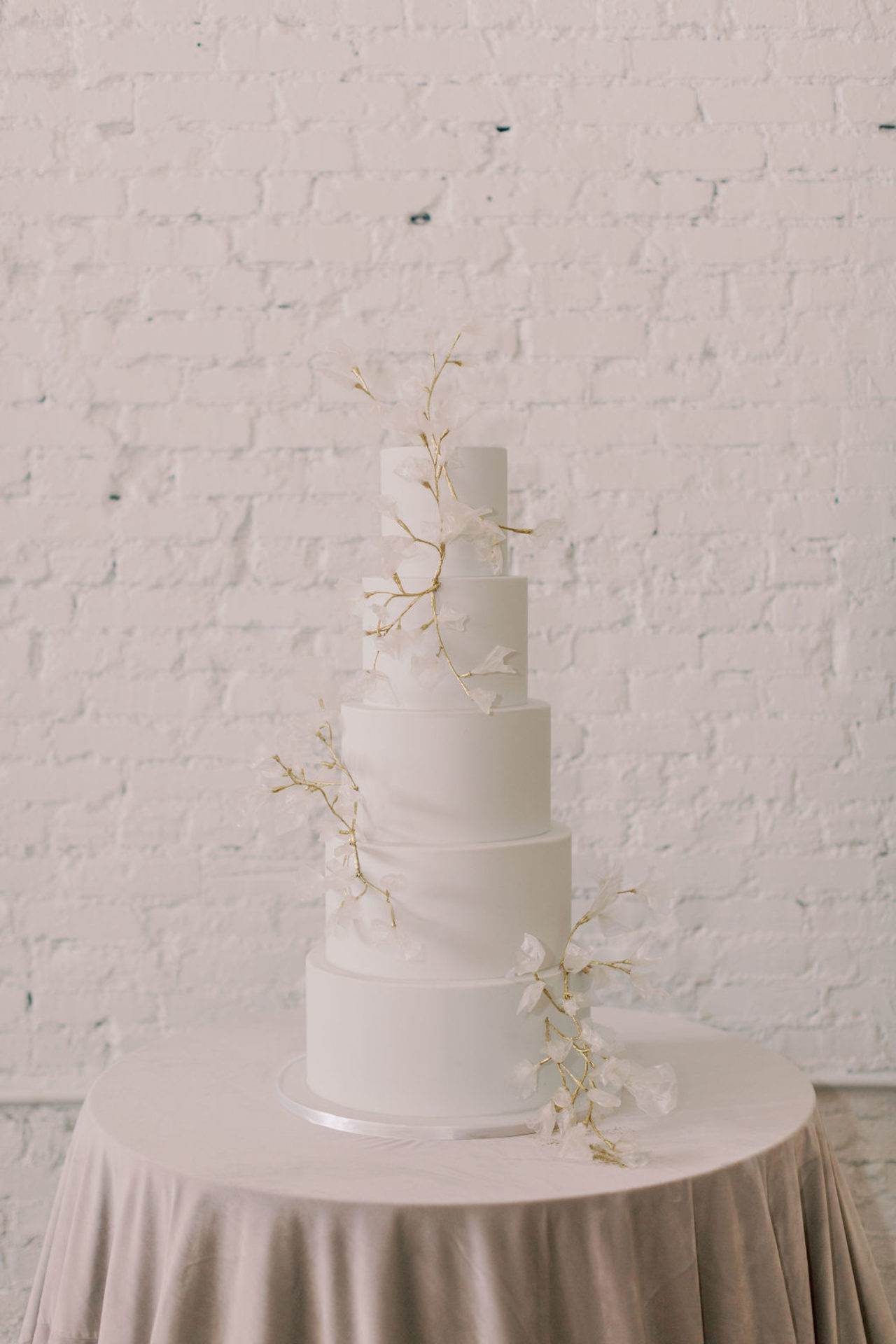 An elegant all white cake in front of a white brick background for a Tampa, FL wedding