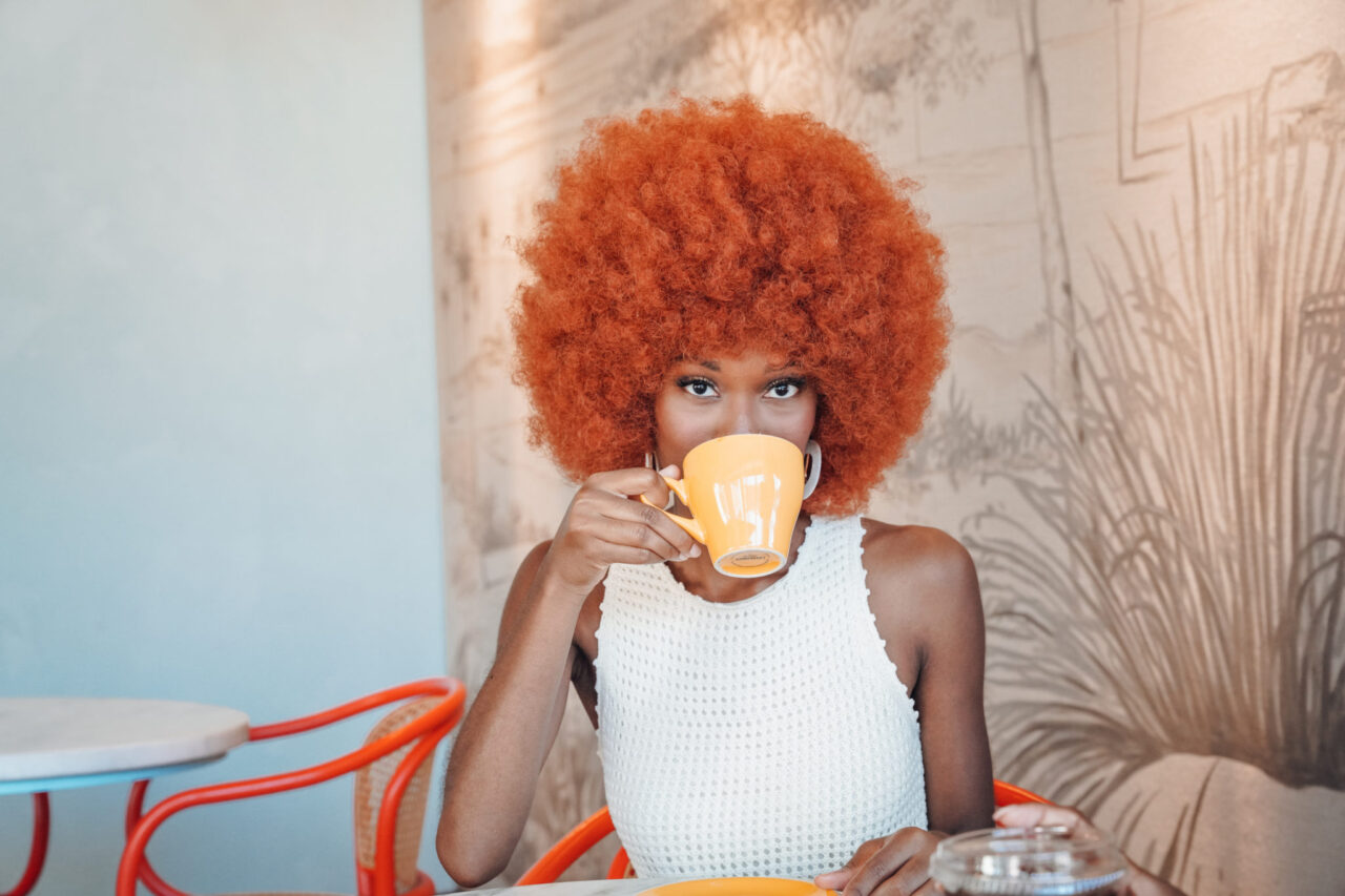 Woman with bright orange afro drinking coffee at our Ybor City, FL hotel