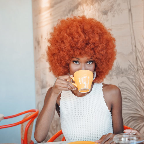 Woman with bright orange afro drinking coffee at our Ybor City, FL hotel